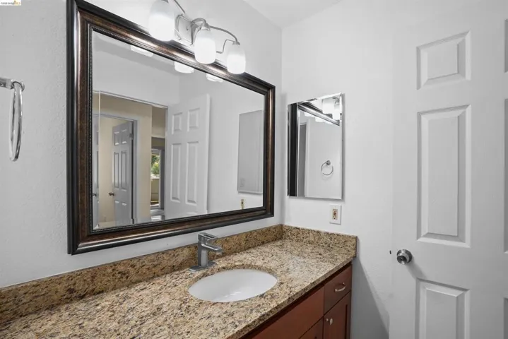 Bathroom vanity featuring a light-toned granite countertop, under-mount sink, and contemporary brushed nickel faucet