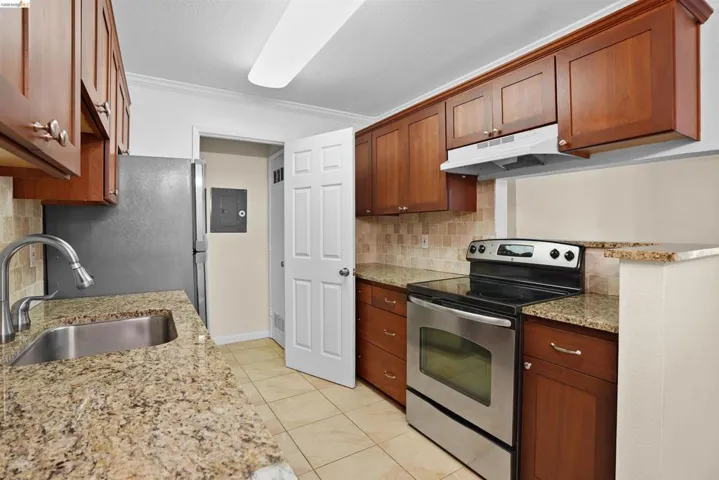 Kitchen featuring wood cabinetry, granite countertops, tile flooring, and stainless steel appliances
