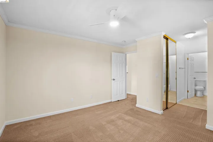 Carpeted bedroom with crown molding, a ceiling fan with integrated lighting, and a mirrored closet
