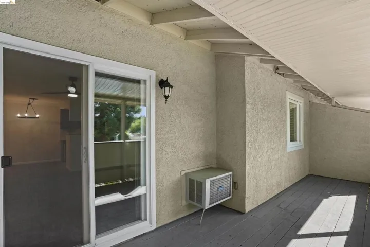 Covered outdoor patio area featuring a textured stucco exterior, sliding glass door, and a single-pane window