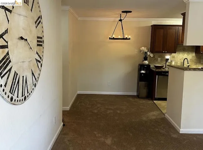 Dining area featuring a chandelier-style light fixture, crown molding, and carpet flooring, with a partial view of a kitchen with dark wood-finish cabinetry, tile backsplash, and a built-in sink