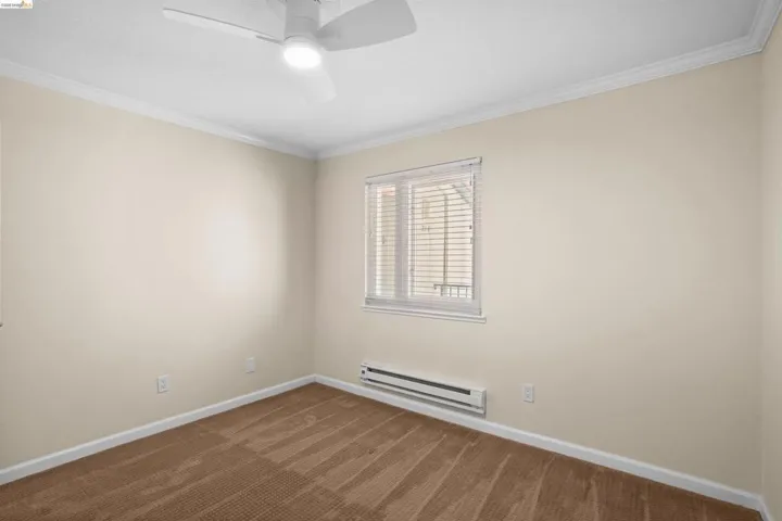 Neutral-toned room featuring a white ceiling fan with integrated lighting, a single window with blinds, baseboard heating, and light brown patterned carpeting