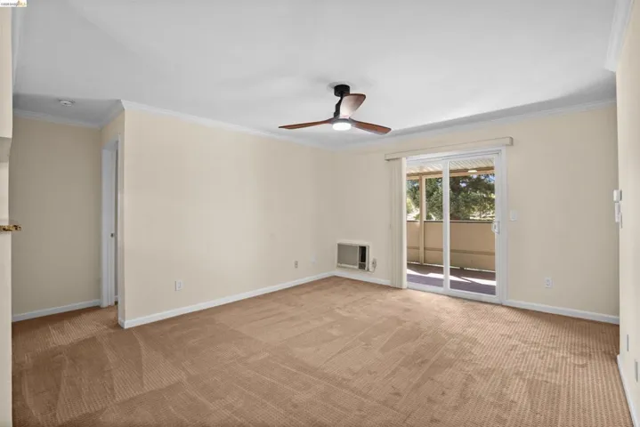 Carpeted interior space featuring a ceiling fan with integrated lighting, crown molding, and an in-wall air conditioning unit