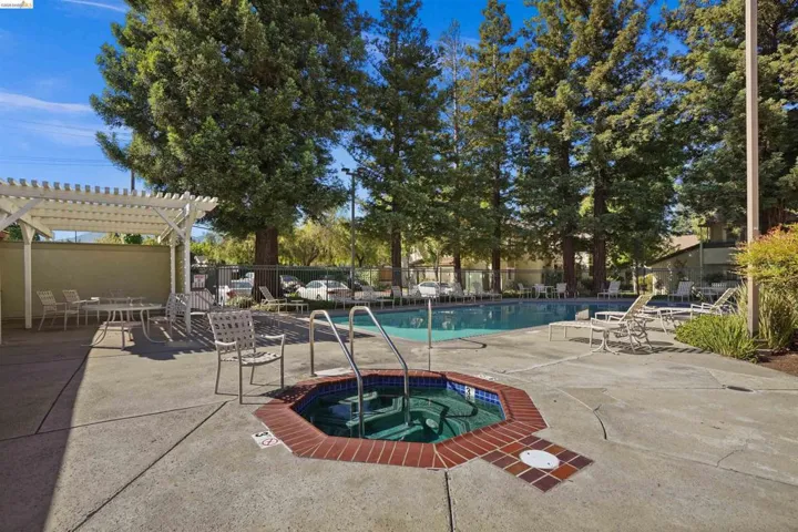 Community pool area featuring a built-in spa with brick coping, an expansive swimming pool, and concrete decking