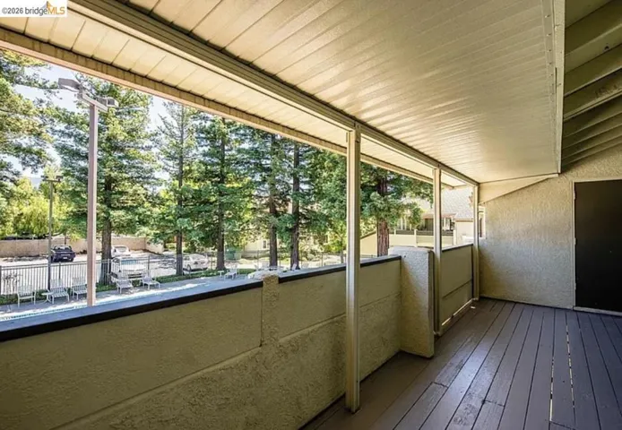 Covered balcony featuring wood-finish flooring, stucco walls, and a private exterior door