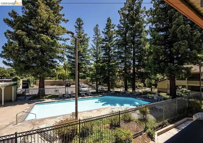 Outdoor swimming pool area featuring a metal perimeter fence, surrounding concrete decking, and multiple lounge chairs
