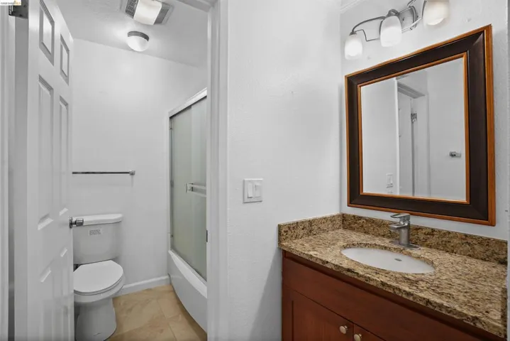 Bathroom featuring a wood-finish vanity with a granite-style countertop, undermount sink, and chrome faucet