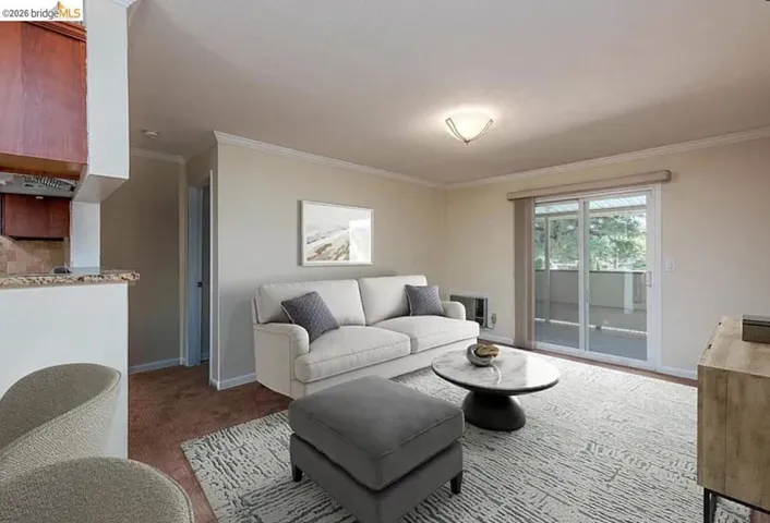 Living area featuring a sliding glass door to an outdoor patio, crown molding, and a built-in kitchen pass-through with a granite countertop and wood cabinetry