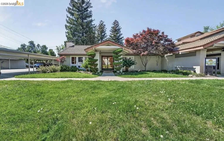 Front exterior featuring a covered entryway, mature landscaping, tiled roof, and an adjacent carport structure
