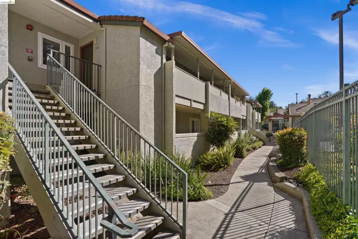 Apartment building exterior featuring stucco siding, terracotta-style roof tiles, and a concrete walkway
