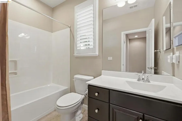 Full bathroom featuring a white tub/shower combination, dark wood-finish vanity with an integrated white sink, a wide wall-mounted mirror, and a window with white louvered shutters