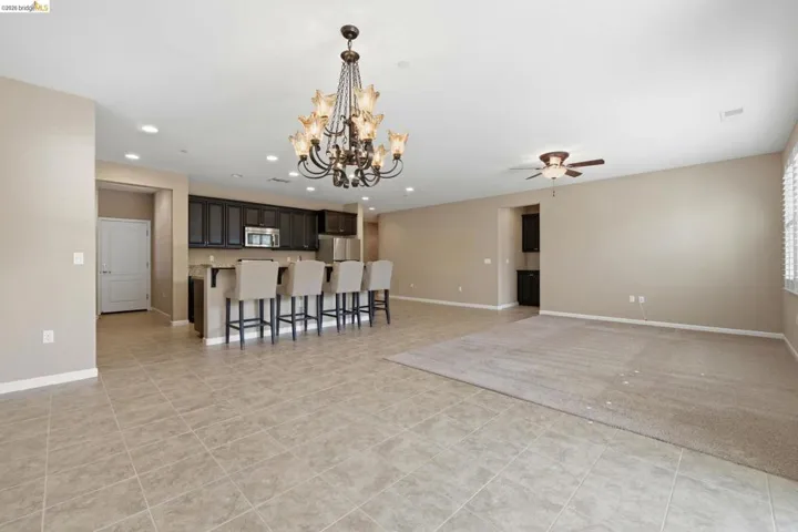 Open-concept living area featuring a kitchen island with seating, dark wood-finish cabinetry, stainless steel appliances, and a decorative chandelier