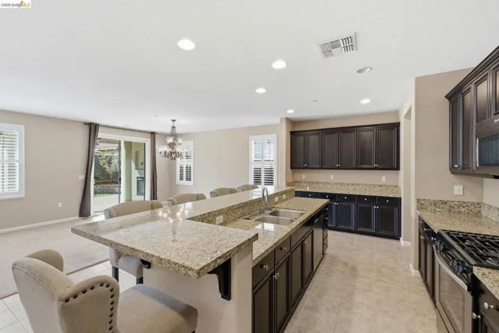 Spacious kitchen featuring dark wood cabinetry, light-toned granite countertops, a double basin undermount sink, and recessed lighting