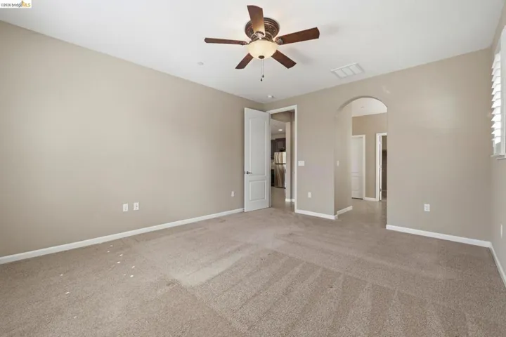 Spacious room featuring neutral carpeting, light neutral wall paint, and a ceiling fan with integrated lighting
