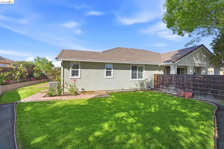 Spacious backyard featuring a manicured lawn, concrete pathway, and raised planter with established foliage