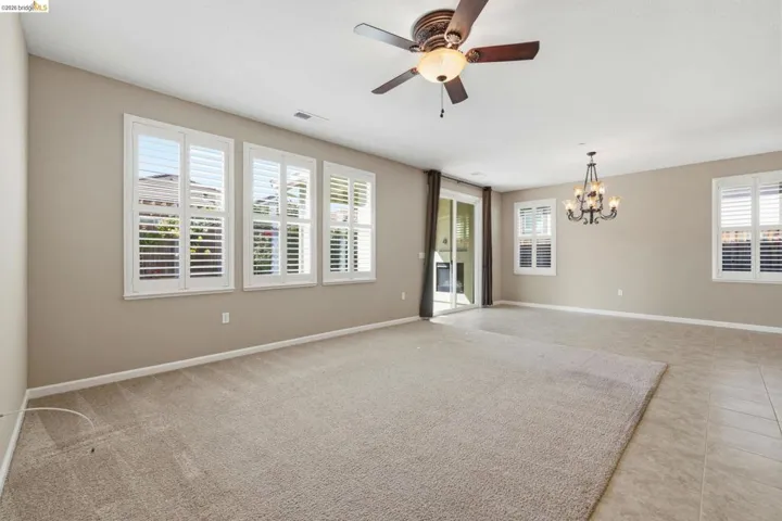 Spacious room featuring multiple windows with louvered shutters, ceiling fan, chandelier, and a sliding glass door