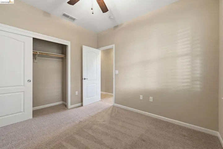 Carpeted room featuring a ceiling fan, a window with horizontal blinds, a closet with bi-fold doors, and a solid interior door