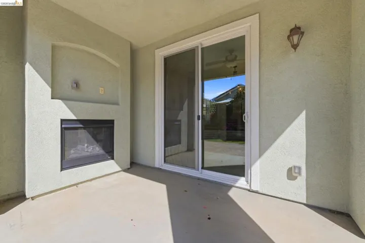 Covered patio featuring an outdoor fireplace with a recessed media niche, a sliding glass door, a wall-mounted light fixture, and a stucco exterior finish