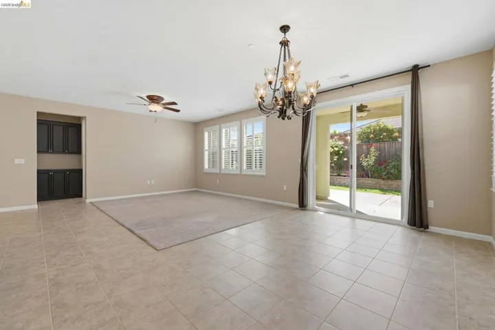 Spacious room featuring neutral tile flooring, a decorative chandelier, and a ceiling fan