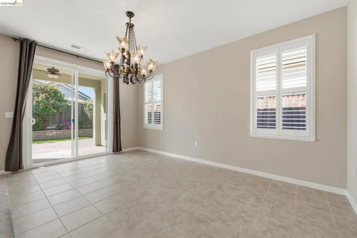 Spacious room featuring neutral wall tones, large format tile flooring, a decorative chandelier, white plantation shutters, and sliding glass doors opening to the backyard
