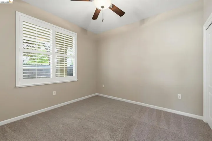 Windowed room featuring neutral-toned walls, plush carpet flooring, a ceiling fan with integrated lighting, and white plantation shutters