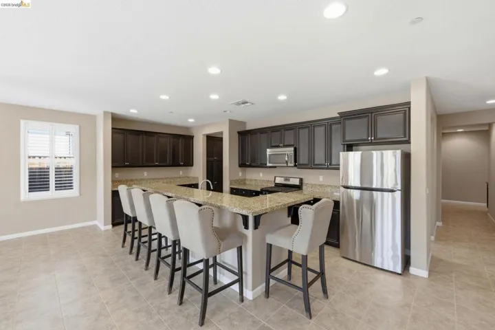 Kitchen featuring an oversized island with seating, dark wood cabinetry, light speckled countertops, and stainless steel appliances