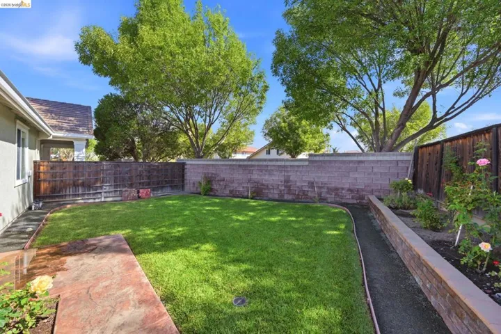 Expansive backyard featuring a lush lawn, concrete block perimeter wall, and a raised planter bed