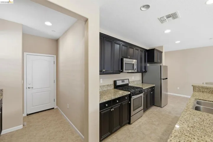 Kitchen featuring dark wood cabinetry, light granite countertops, stainless steel appliances, and recessed lighting