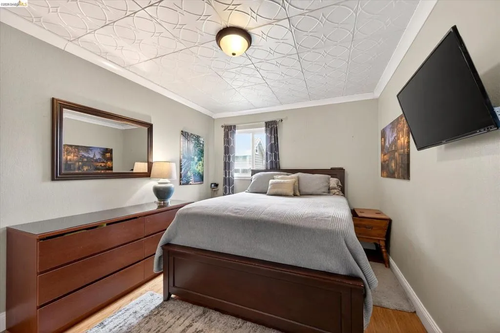 Bedroom featuring a patterned ceiling, crown molding, and wood-finish flooring