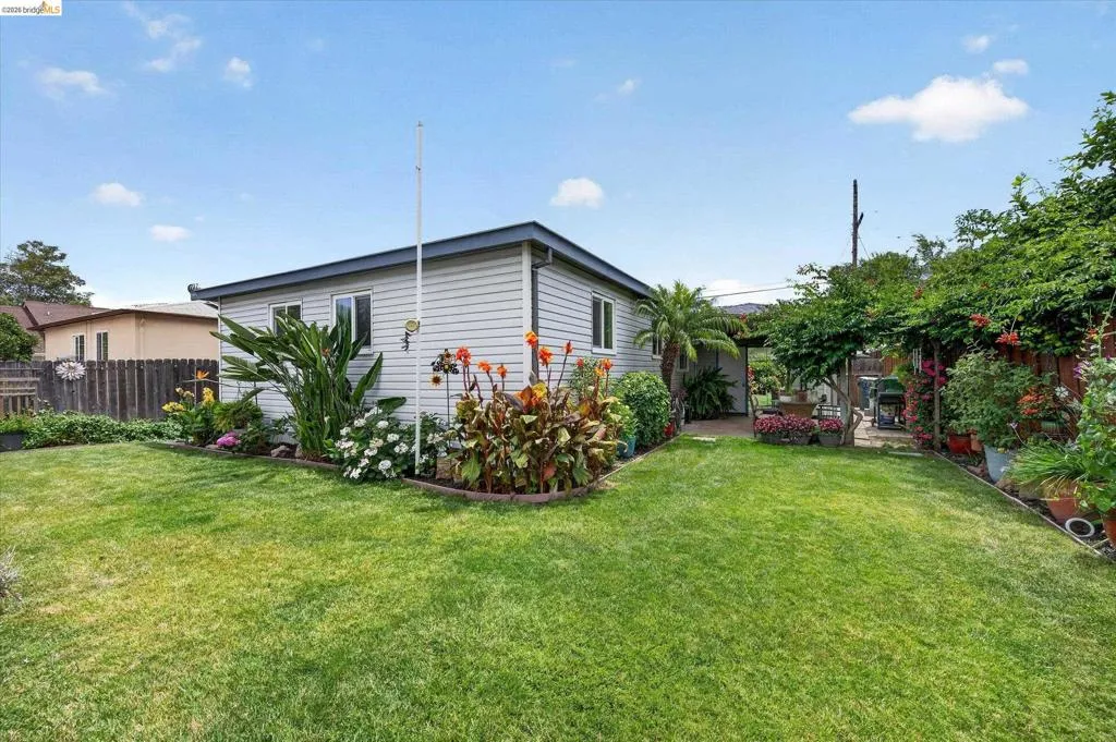 Spacious backyard featuring a lush lawn, established garden beds with various plantings, and a covered patio area