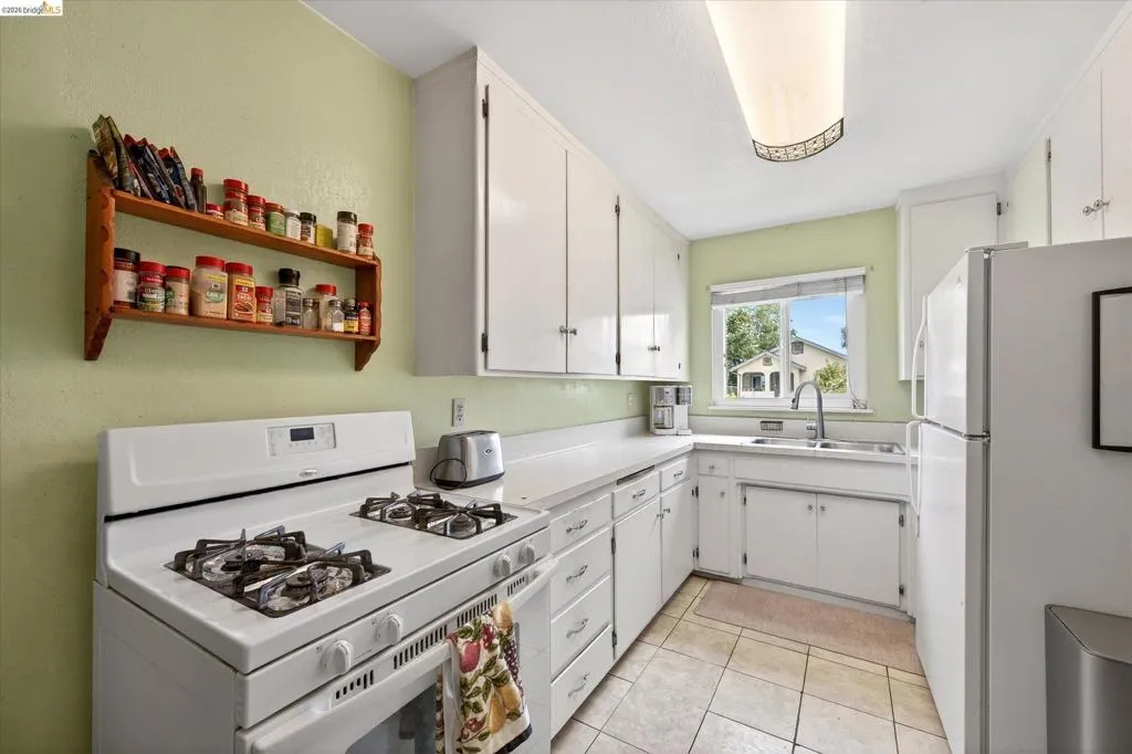 Efficient kitchen featuring white cabinetry, a gas range, stainless steel sink, and durable tile flooring