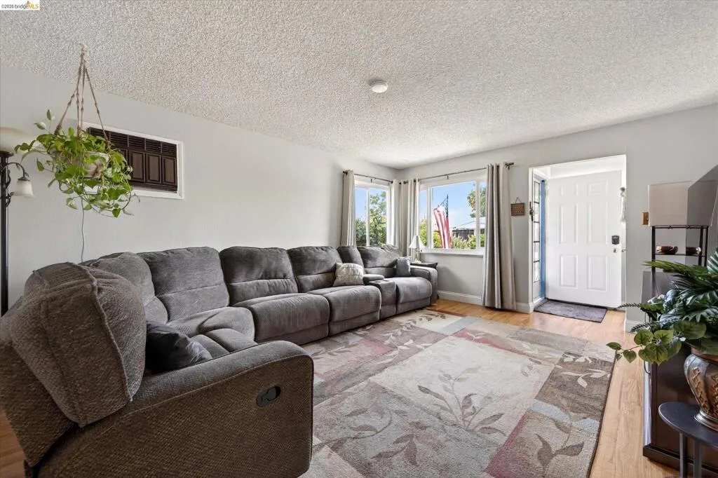 Spacious living area featuring wood-finish flooring, light grey wall paint, and multiple windows allowing natural light