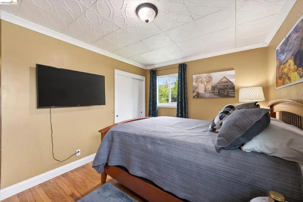 Bedroom featuring hardwood-finish flooring, a decorative ceiling, and a window with garden views