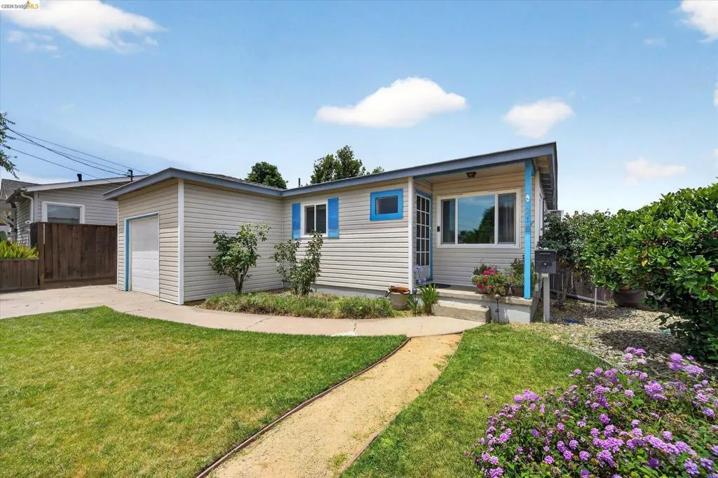 Ranch-style exterior with horizontal siding, an attached garage, a covered entry, established landscaping, and a curvilinear pathway