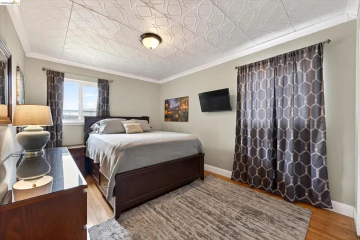 Bedroom featuring wood-finish flooring, a decorative patterned ceiling, and crown molding