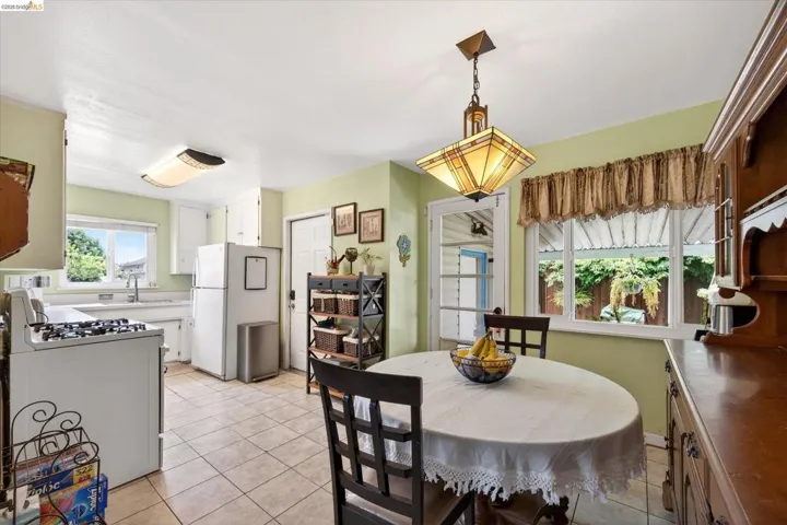 Efficient kitchen and dining area featuring tiled flooring, white cabinetry, a built-in oven range, and a window overlooking exterior greenery