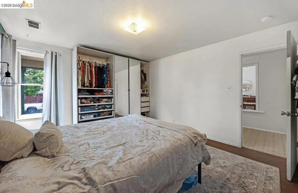 Bedroom featuring wood-finish flooring, a window with curtains, and a built-in closet system with shelving and drawers