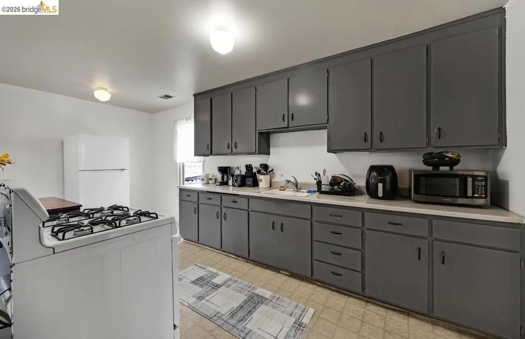 Kitchen featuring extensive grey cabinetry with ample storage, white countertops, and white appliances including a refrigerator and range