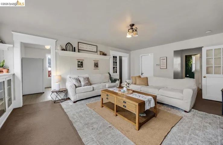 Bright living area featuring light-toned walls and ceiling, brown carpet flooring, and white trim