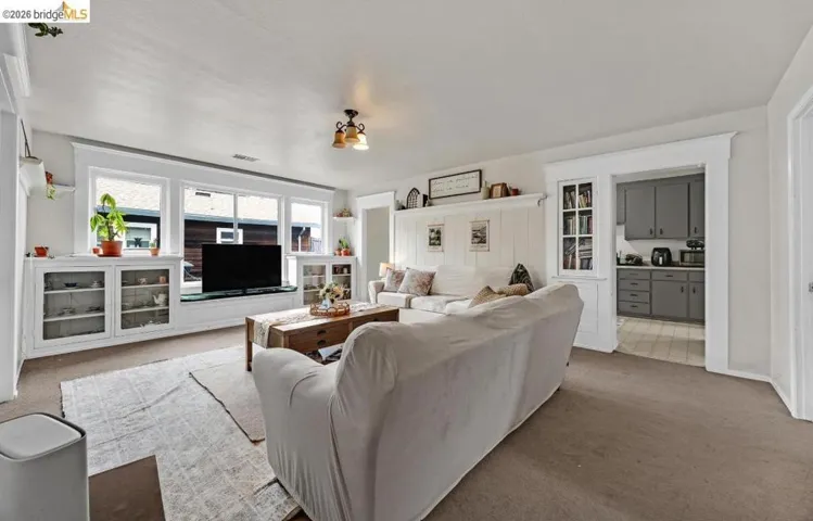Bright living space featuring multiple windows with integrated window seating, built-in cabinetry with glass panel doors, and neutral carpeting