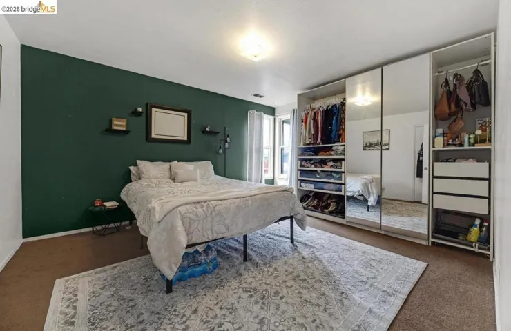 Bedroom featuring a prominent deep green accent wall, wall-to-wall carpeting, and a built-in wardrobe with mirrored doors