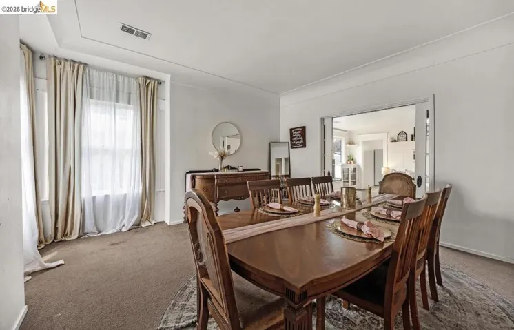 Bright dining area featuring a window with sheer and solid curtains, white crown molding, and a wide cased opening to an additional room