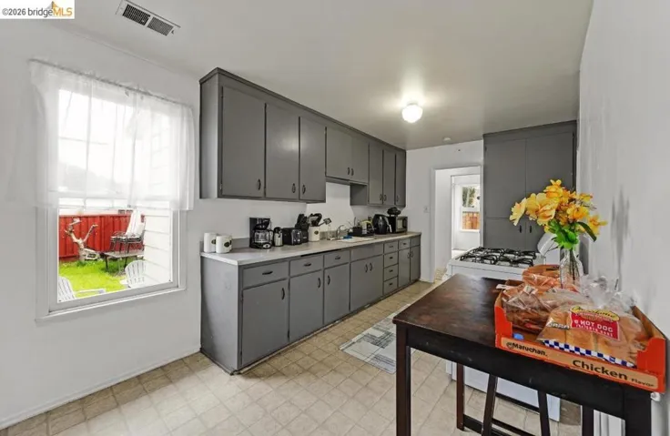 Kitchen featuring gray cabinetry, light countertops, a gas range, tile flooring, and a window overlooking a fenced yard