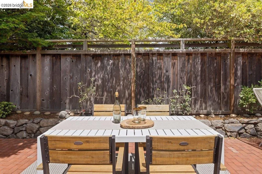 Brick patio featuring a wooden privacy fence, stone retaining wall, and mature landscaping