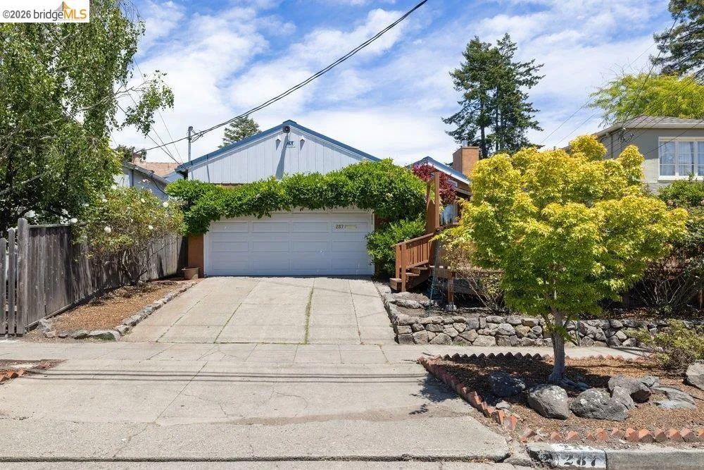 Front exterior featuring a white garage door, a sloped driveway, and mature landscaping