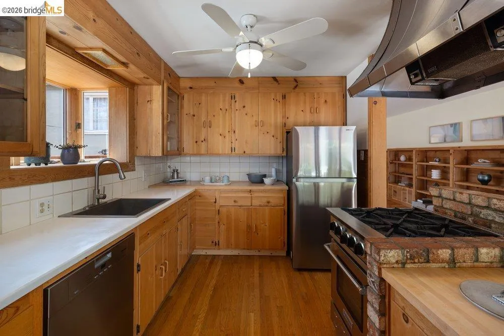 Kitchen featuring wood-finish flooring and cabinetry, stainless steel appliances, a ceiling fan, and white countertops