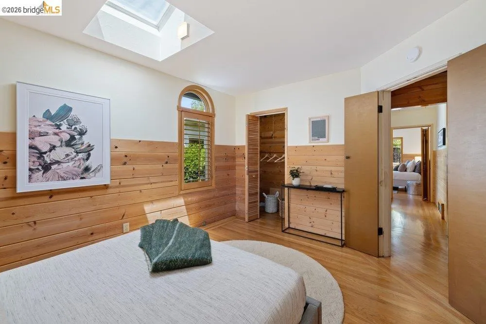 Bedroom featuring wood-finish flooring, a skylight, and partial wood-paneled walls