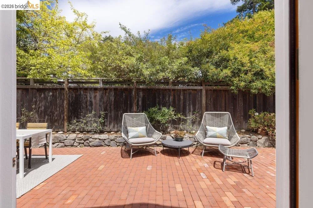 Brick paver patio featuring a wooden privacy fence, stone retaining wall, and mature trees