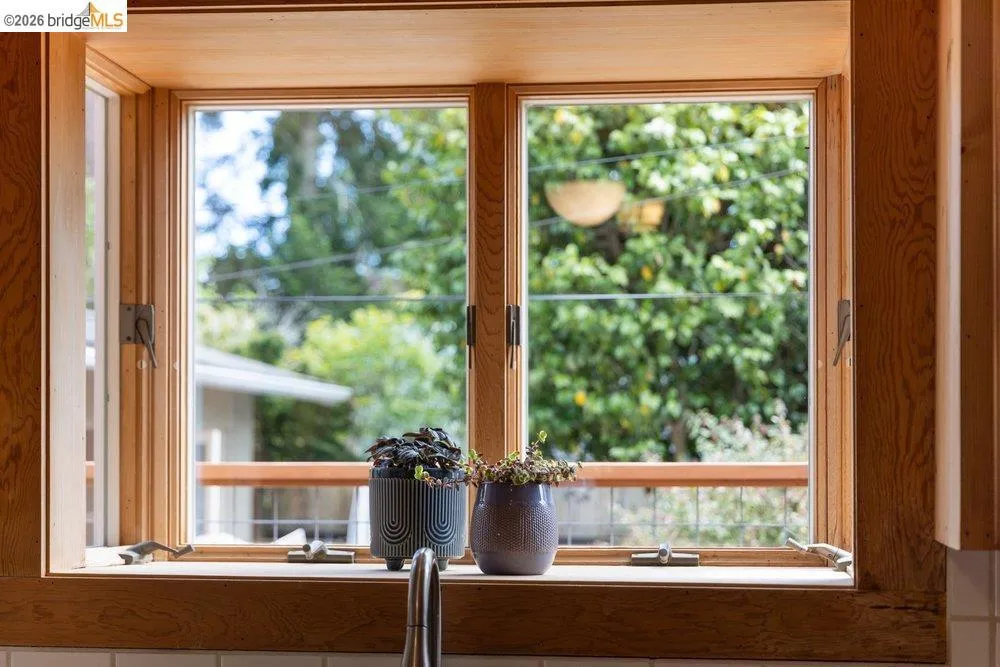 Double-hung casement windows featuring natural wood framing and trim above a white tile backsplash and a stainless steel faucet