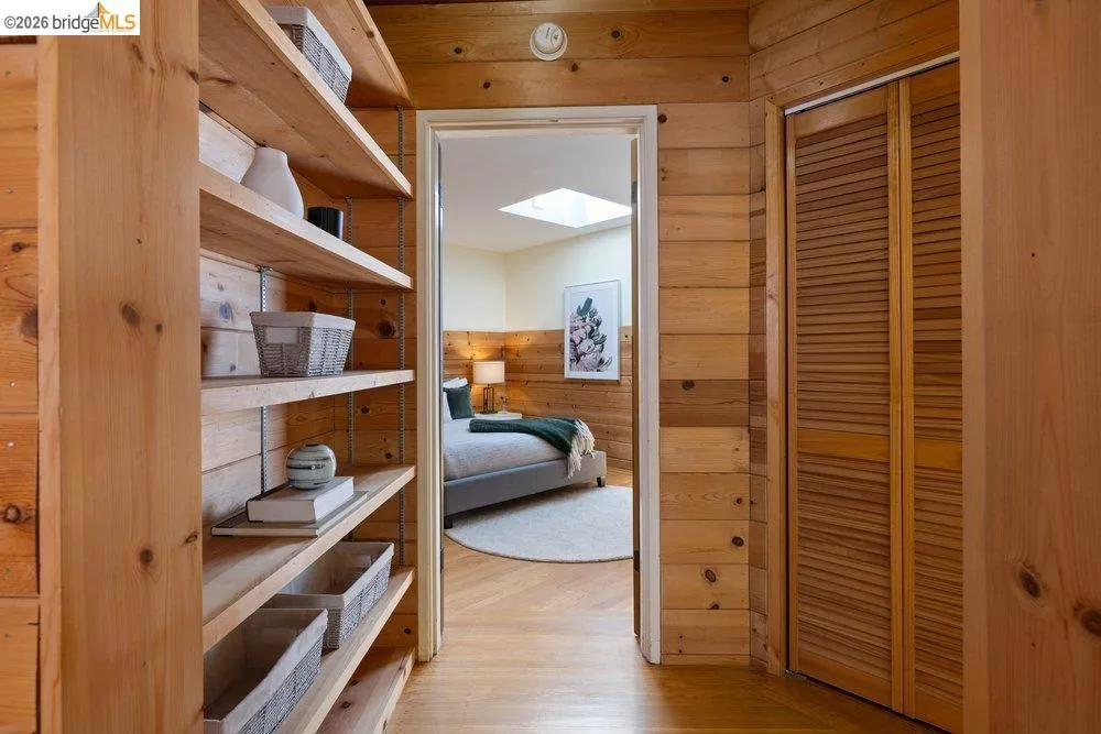Wood-paneled hallway featuring built-in shelving, louvered closet doors, and hardwood flooring